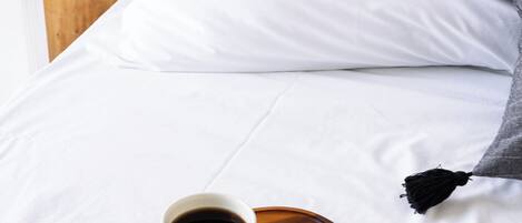A neatly made bed with white linens, a cup of coffee on a wooden tray, and a bedside lamp.