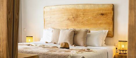 Ein ordentlich bezogenes Bett mit einem Holz-Kopfteil, zwei Nachttischlampen und einem gewebten Korb auf dem Bett.