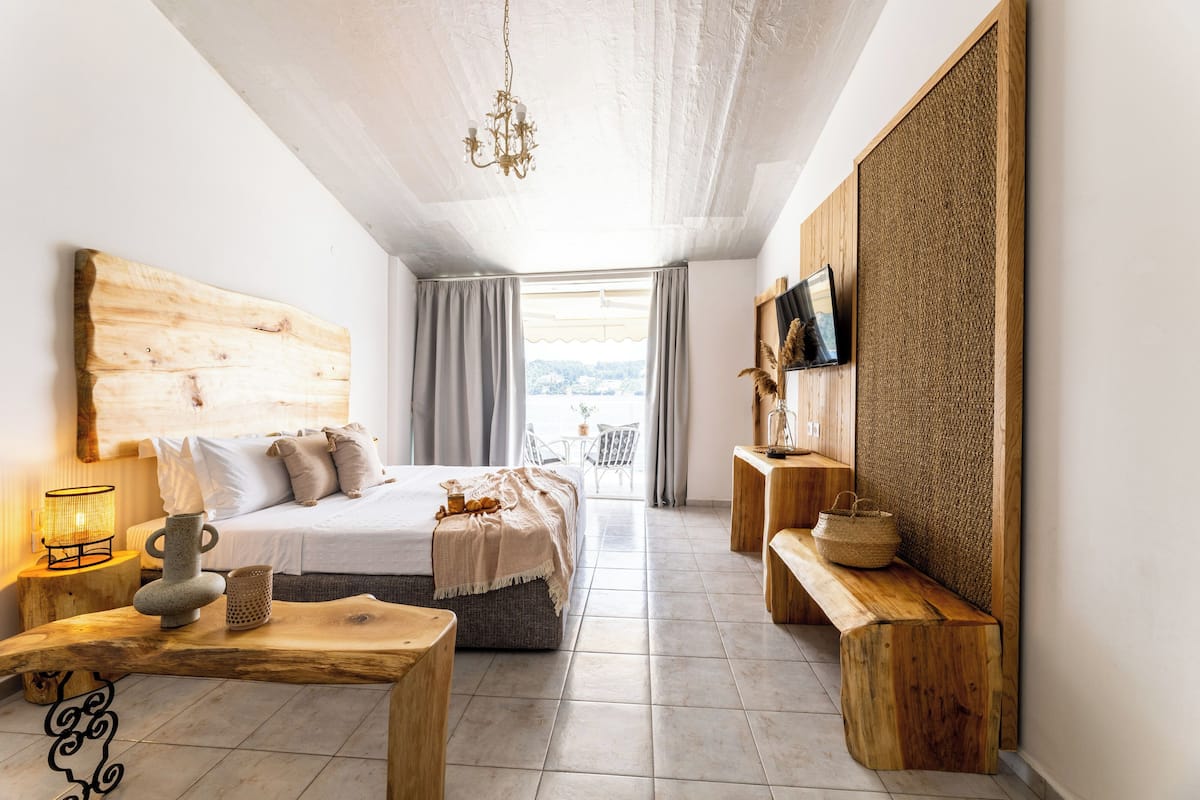 A bedroom with a large bed, wooden headboard, bedside tables, a TV, and a view of the outdoors.