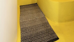 A bathroom with a yellow wall, a framed artwork, a bathtub, and a patterned rug. - Casa Blue Marine (Skiathos)