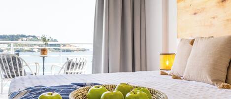 Una cama con una cesta de manzanas verdes, vista al mar y una lámpara en una mesita de noche.