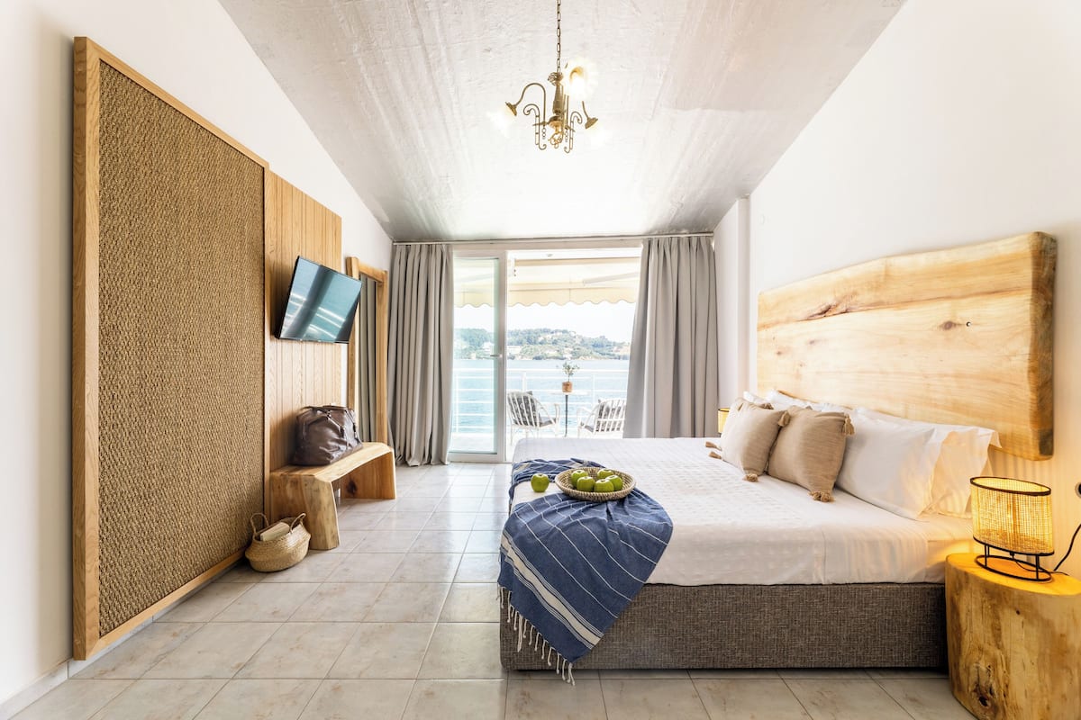 A bedroom with a large bed, a television, a wooden headboard, a bench, and a view of the outdoors.