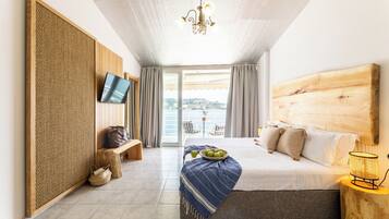 A bedroom with a large bed, a television, a wooden headboard, a bench, and a view of the outdoors.