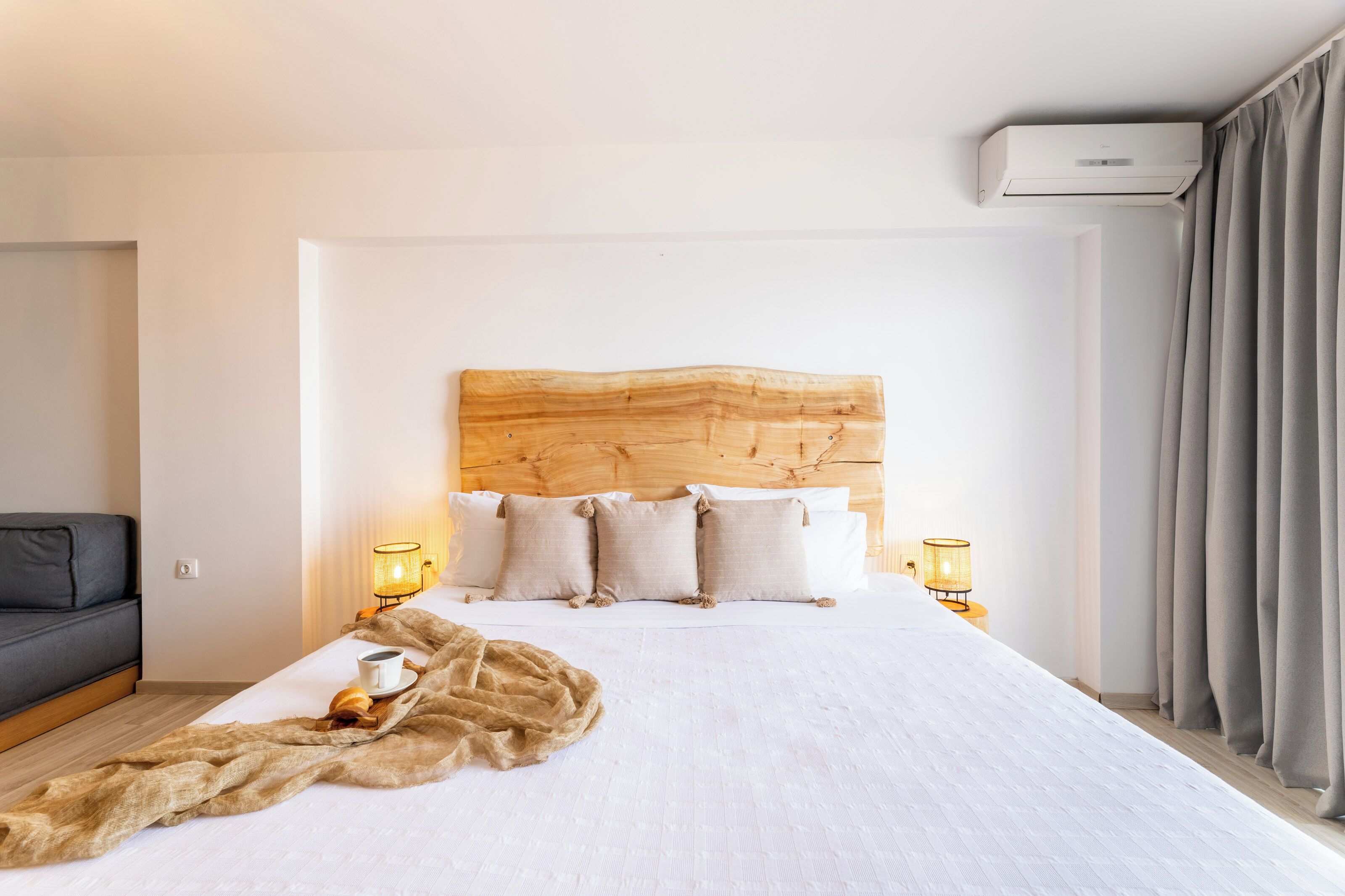 A hotel room with a wooden headboard, white bedding, two bedside lamps, and a fur throw on the bed.