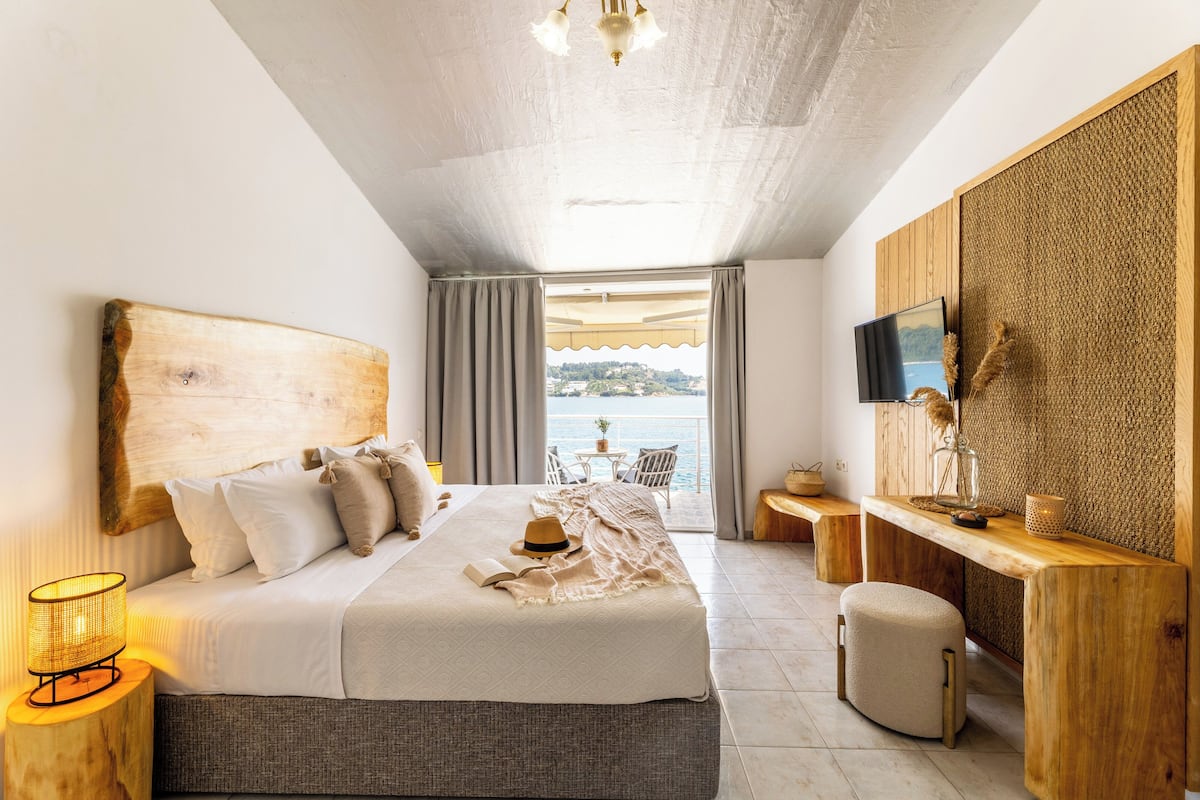 A bedroom with a large bed, a bedside table, a TV, and a view of the sea.