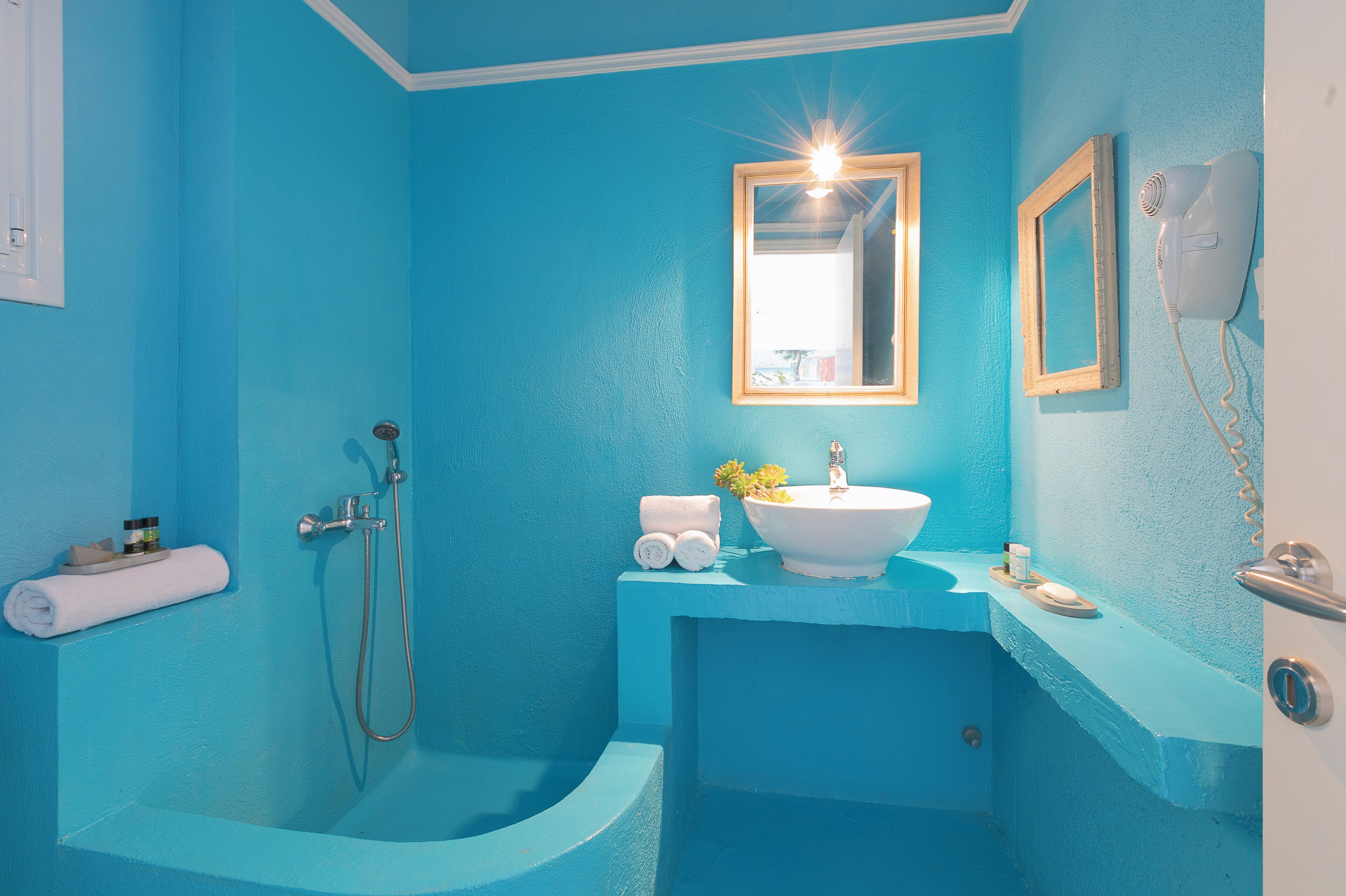 Un baño con pared azul, lavamanos blanco, espejo y secador de pelo.