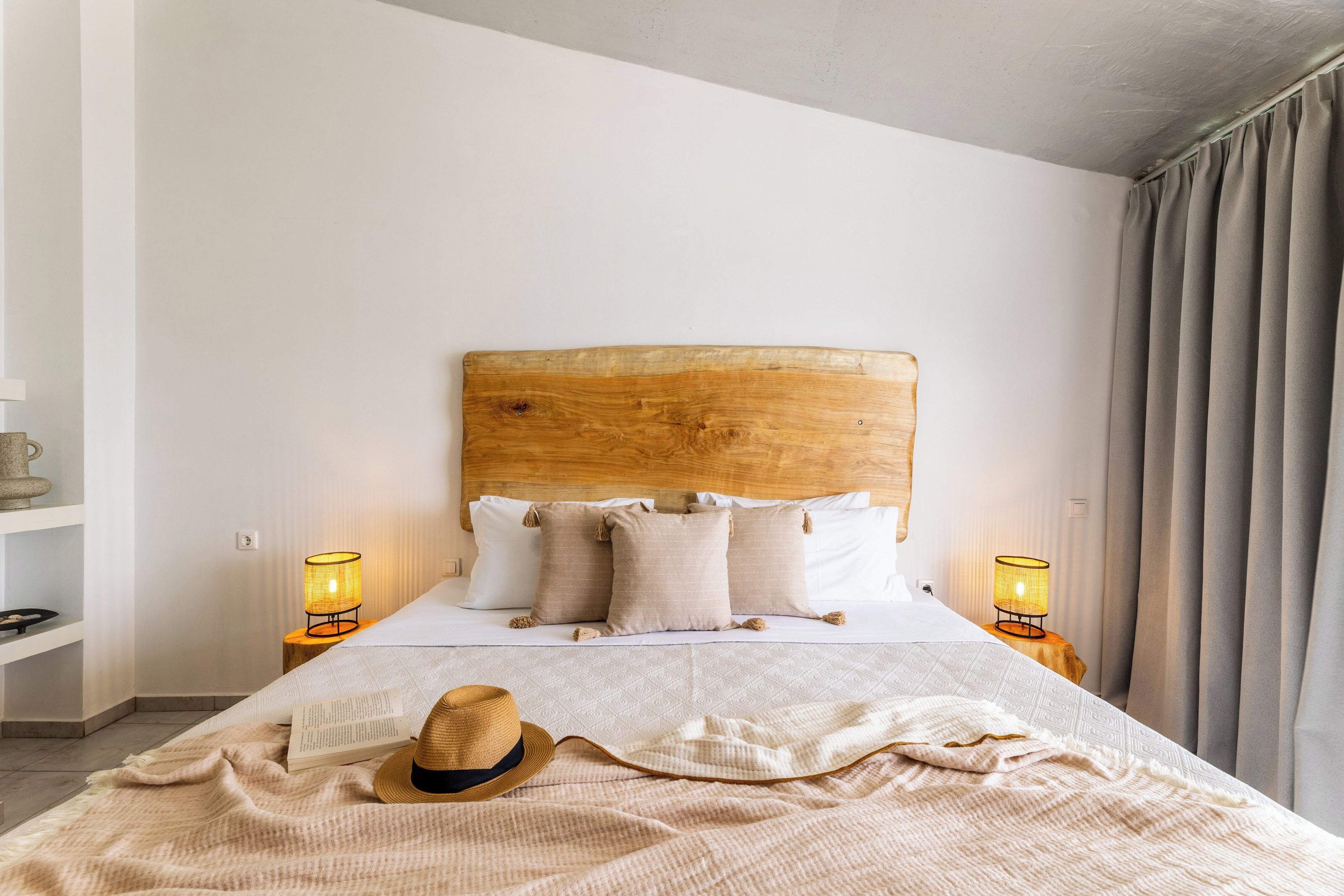 Una cama bien hecha con cabecera de madera, dos lámparas de noche y un sombrero sobre la cama.
