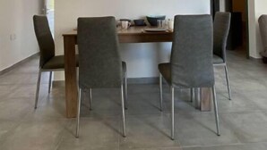 A dining area with a rectangular table, four grey chairs, and wall-mounted lighting. - Two bedroom apt with terrace in center ayia napa. (Ayia Napa)
