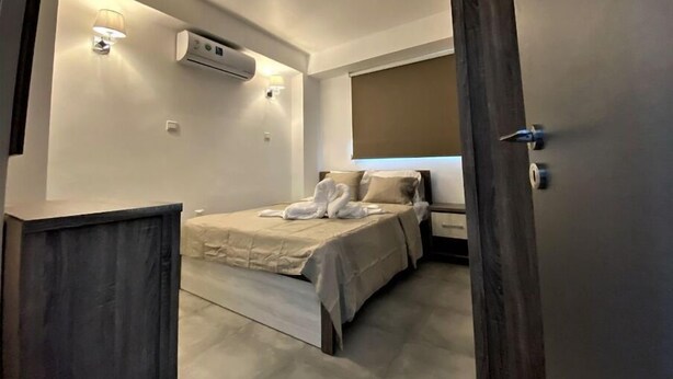 A modern hotel room with a bed, two wall-mounted lights, an air conditioning unit, and a window with a blind. - Two bedroom apt with terrace in center ayia napa. (Ayia Napa)