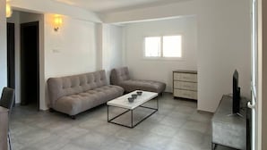 A modern living room with a sectional sofa, a coffee table, a TV stand, and a window providing natural light. - Two bedroom apt with terrace in center ayia napa. (Ayia Napa)