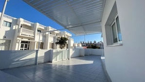 A covered outdoor area with a tiled floor, a white building with balconies, and a clear blue sky. - Two bedroom apt with terrace in center ayia napa. (Ayia Napa)