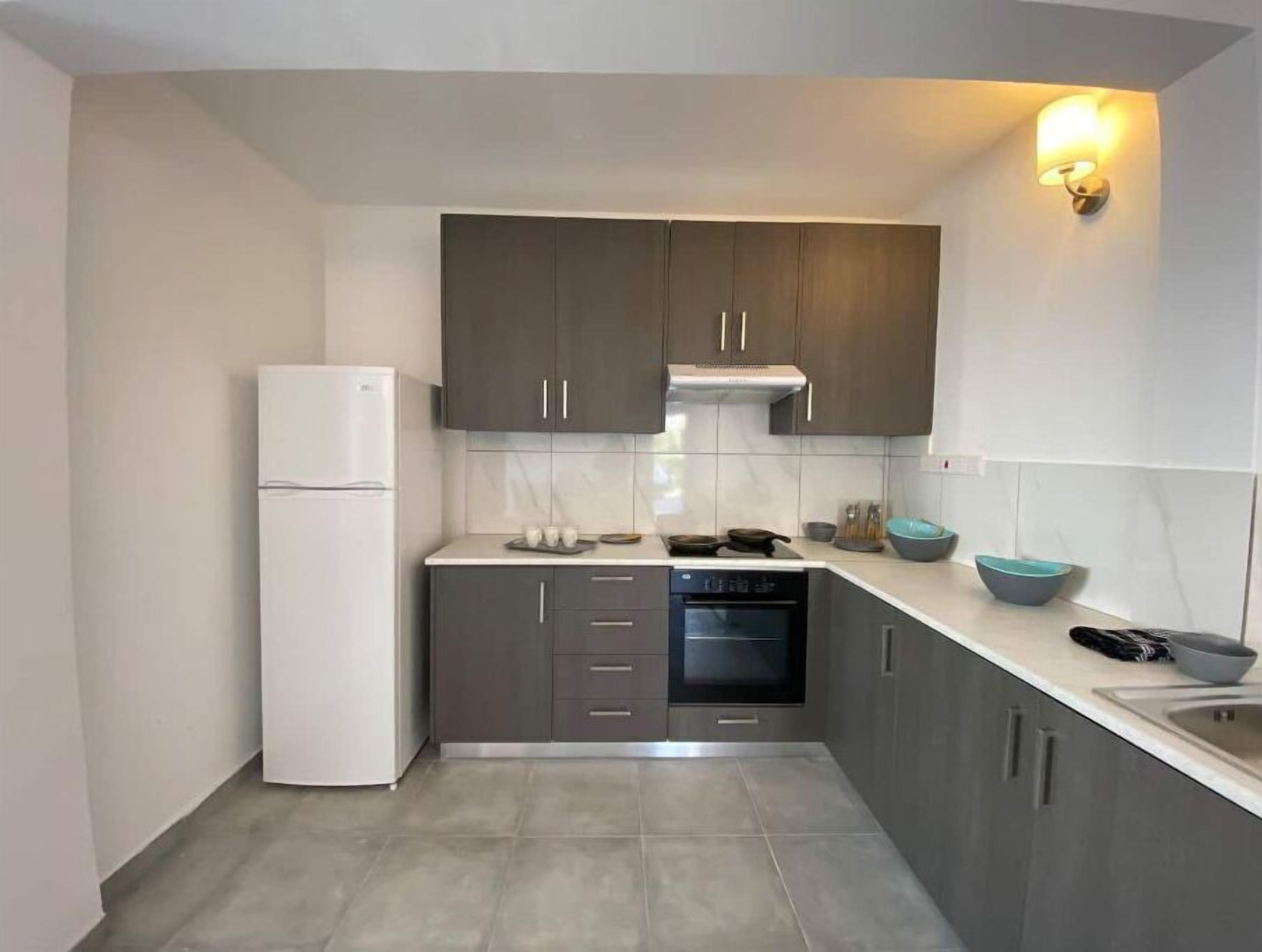 A compact kitchen with dark cabinets, a white refrigerator, and a built-in oven.