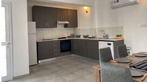 A modern kitchen with dark cabinets, a dishwasher, and a dining area with a table and chairs. - Two bedroom apt with terrace in center ayia napa. (Ayia Napa)