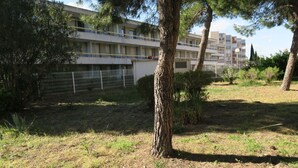 A multi-story building with balconies, surrounded by trees and a fenced area.