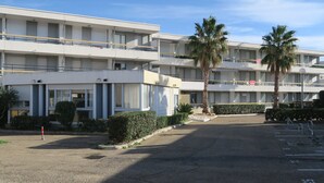 A multi-story hotel with balconies, palm trees, and a parking area.