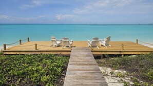 A wooden pier leading to a beach with white chairs and a clear view of the turquoise sea. - Seas The Day (Georgetown)