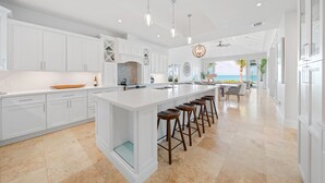 A modern kitchen with white cabinetry, a large island with stools, and a view of the ocean. - Seas The Day (Georgetown)