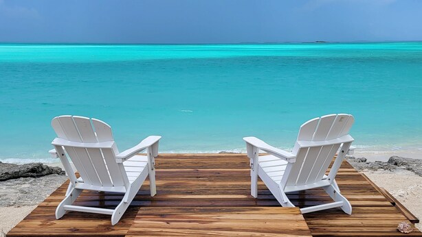 Two white Adirondack chairs facing a wooden deck with a view of turquoise ocean waters. - Seas The Day (Georgetown)