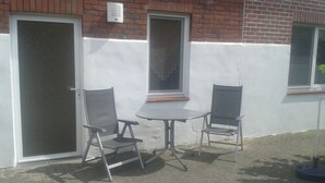 An outdoor seating area with two chairs and a table, adjacent to a building with a white and red brick facade. - Vacation home Gerken - Apartment on the first floor (Drochtersen)