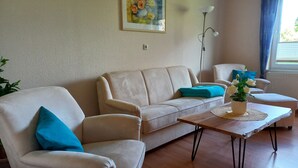 A living room with a beige sofa, a wooden coffee table, and a potted plant. - Vacation home Gerken - Apartment on the first floor (Drochtersen)