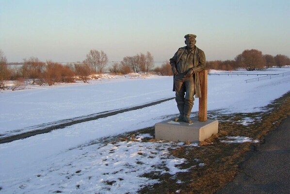 Une statue représentant un homme en costume et chapeau, debout sur un piédestal, au bord d’une route.