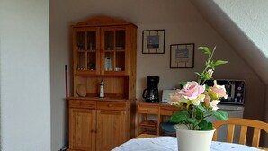 A dining area with a wooden table, chairs, a white tablecloth, a potted plant, and a wooden cabinet with glass doors. - Vacation home Gerken - Apartment in the attic (Drochtersen)