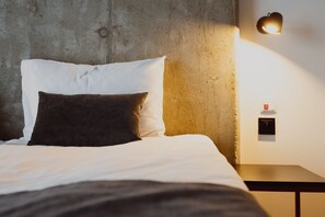 A bed with white and dark pillows, a bedside table, and a wall-mounted light fixture. - Arche Hotel Piła (Pila)
