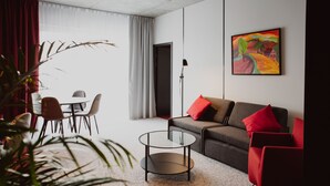 Una sala de estar moderna con un sofá gris, cojines rojos, una mesa de centro de vidrio y un comedor con sillas y una mesa.