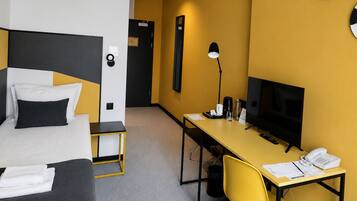 Quarto de hotel com cama, escrivaninha, cadeira, televisão e telefone.