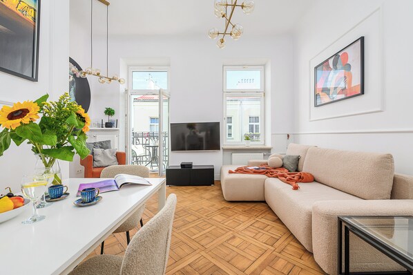 A modern living room with a sofa, TV, and a dining area with a table and chairs. - ShortStayPoland Poznańska B23 (Warsaw)