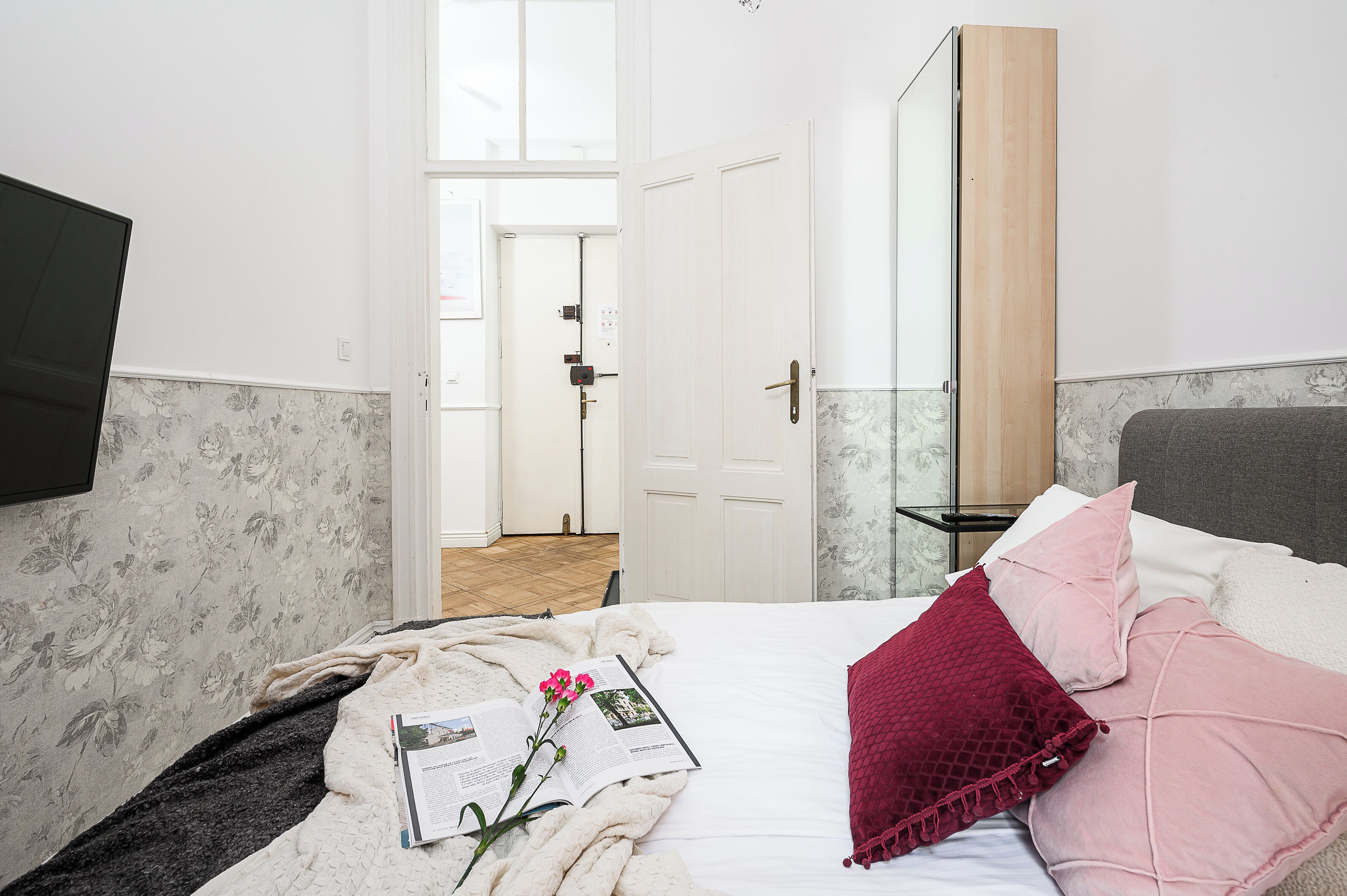 Un dormitorio con cama, mesita de noche, espejo y puerta que da a otra habitación.