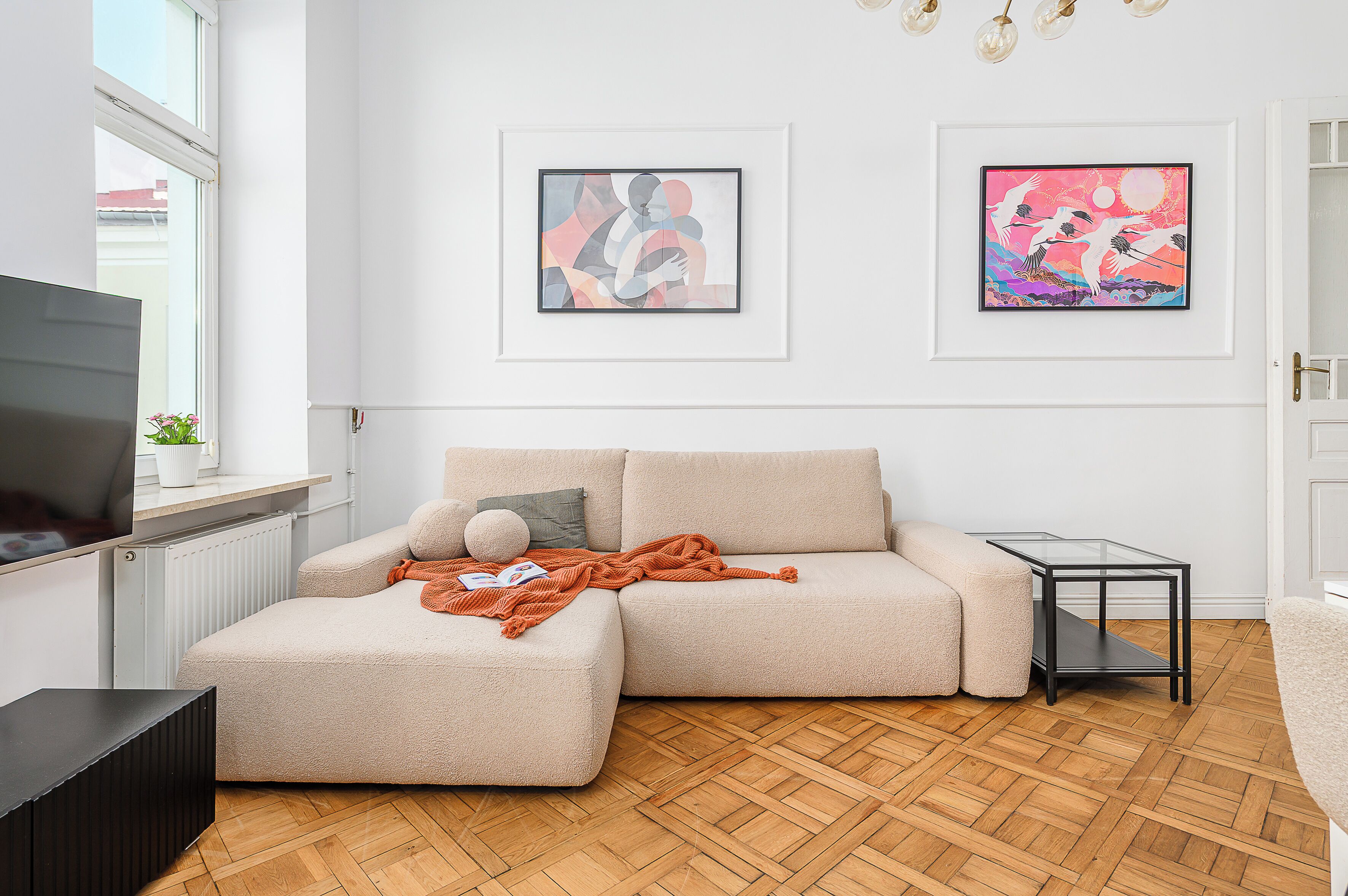 Een moderne woonkamer met een modulaire bank, een glazen salontafel en twee kunstwerken in lijsten aan de muur.