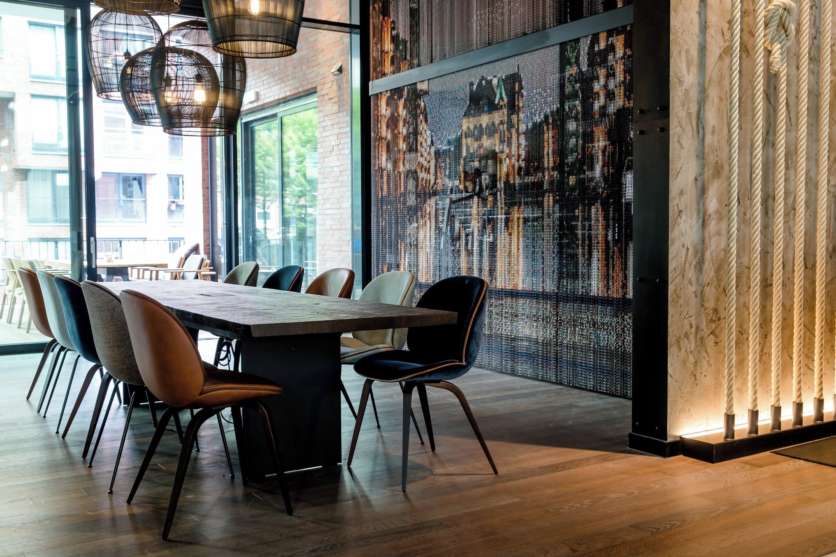 A modern dining area with a long table, chairs, and a cityscape mural on the wall.
