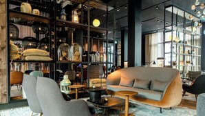 Een modern interieur met een bank, fauteuils, een bijzettafeltje en een boekenkast vol diverse spullen.