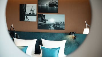 A hotel room with a bed, pillows, a wall-mounted lamp, and three framed photographs of industrial scenes.