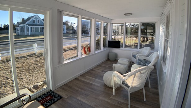 A sunroom with large windows, wicker furniture, and a flat-screen TV. - Lower County Bunk House (Dennis)
