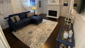 A living room with a dark blue sectional sofa, a patterned rug, a white fireplace, and a blue side table with decorative vases. - Lower County Bunk House (Dennis)