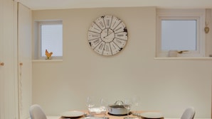 Een eetruimte met een ronde wandklok, een houten tafel gedekt voor vier personen en een raam met uitzicht.