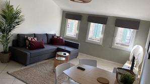 A modern living room with a grey sofa, a dining table, and a large potted plant. - APPART NOE - rue Carreterie - 4 pers. (Avignon)