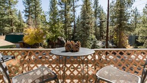 A balcony with a round table and two chairs, surrounded by a lattice fence. - Cute Cozy Cabin- View of the Slopes-Pets OK! (Big Bear Lake)