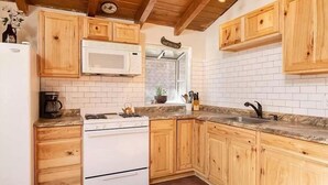 A kitchen with wooden cabinets, a white stove, a microwave, and a sink. - Cute Cozy Cabin- View of the Slopes-Pets OK! (Big Bear Lake)
