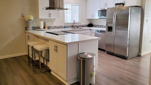 A modern kitchen with white cabinetry, a stainless steel refrigerator, and a central island with bar stools. - Condo *Zen* King N. Phoenix 30 (Phoenix)