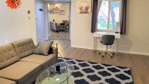 A living room with a sofa, coffee table, and a patterned rug. There is a desk with a chair and a window with curtains. - Condo *Zen* King N. Phoenix 30 (Phoenix)