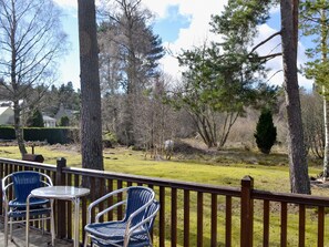 A deck with two wicker chairs and a small table, overlooking a grassy yard with trees and a distant house.