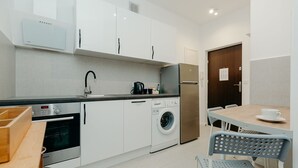 Una cocina compacta con muebles blancos, horno Bosch, lavadora y comedor con mesa y sillas.