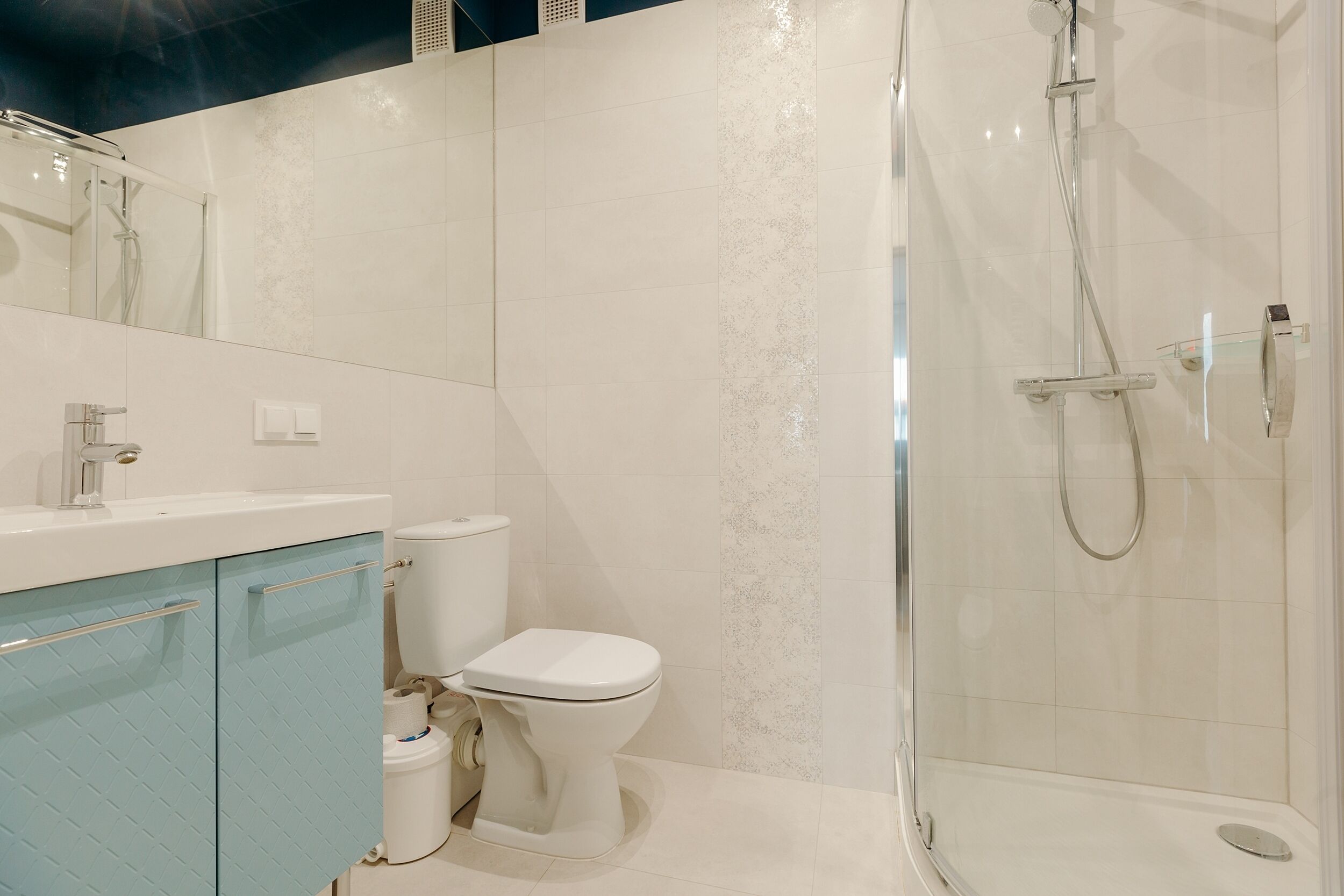 Un bagno moderno con box doccia in vetro, un water bianco e un armadietto blu.
