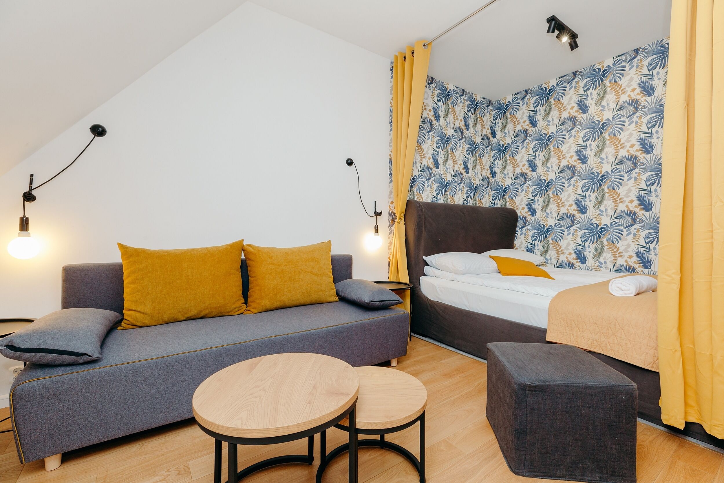 A modern, compact room with a sofa, a bed, a small table, and a bench.
