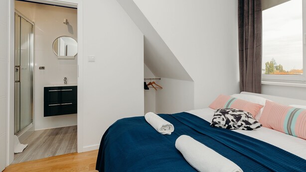 Un dormitorio con cama, ventana, baño con espejo y ducha.