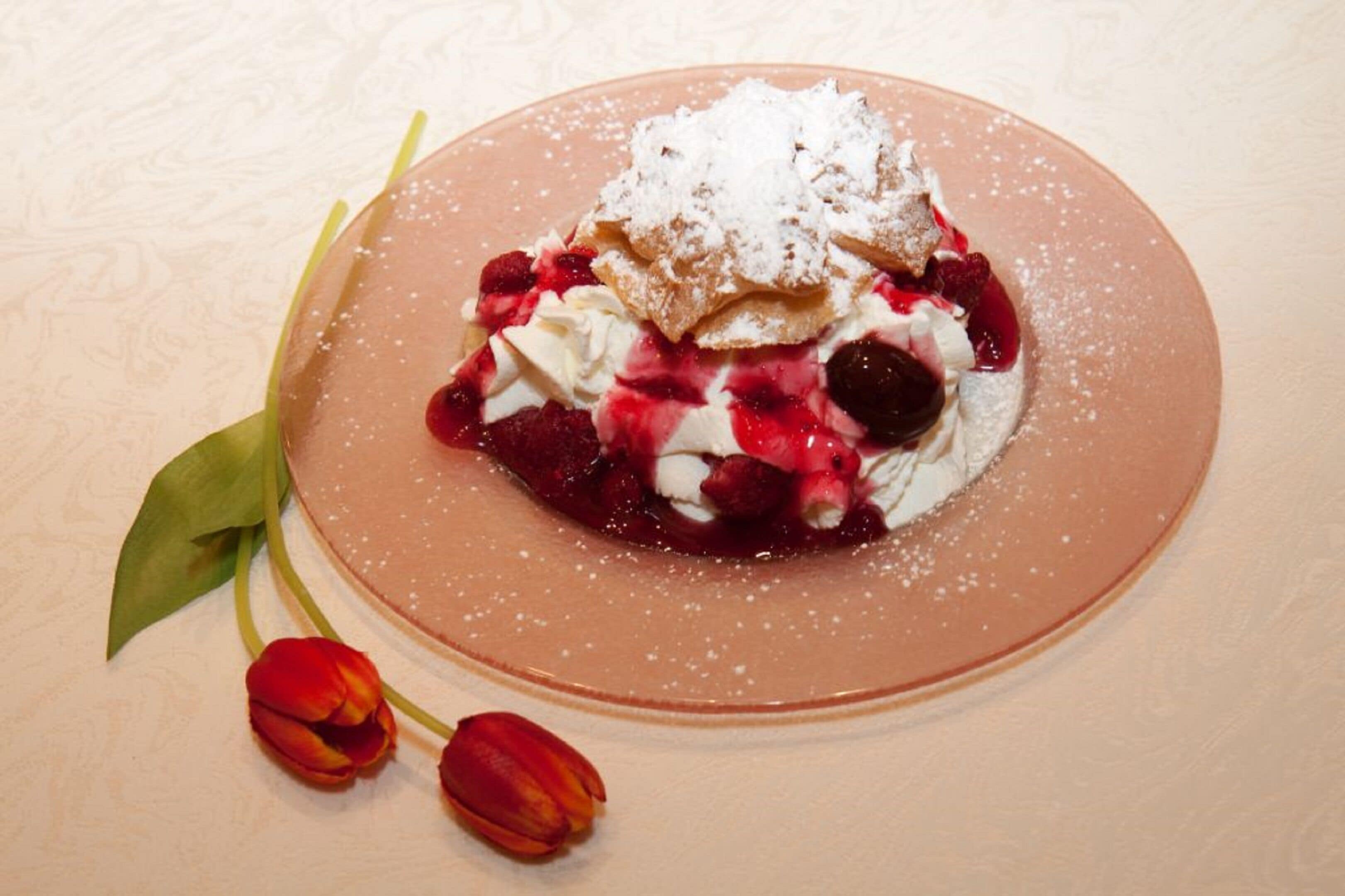 Un postre en un plato con azúcar glas, frutos rojos y crema batida.