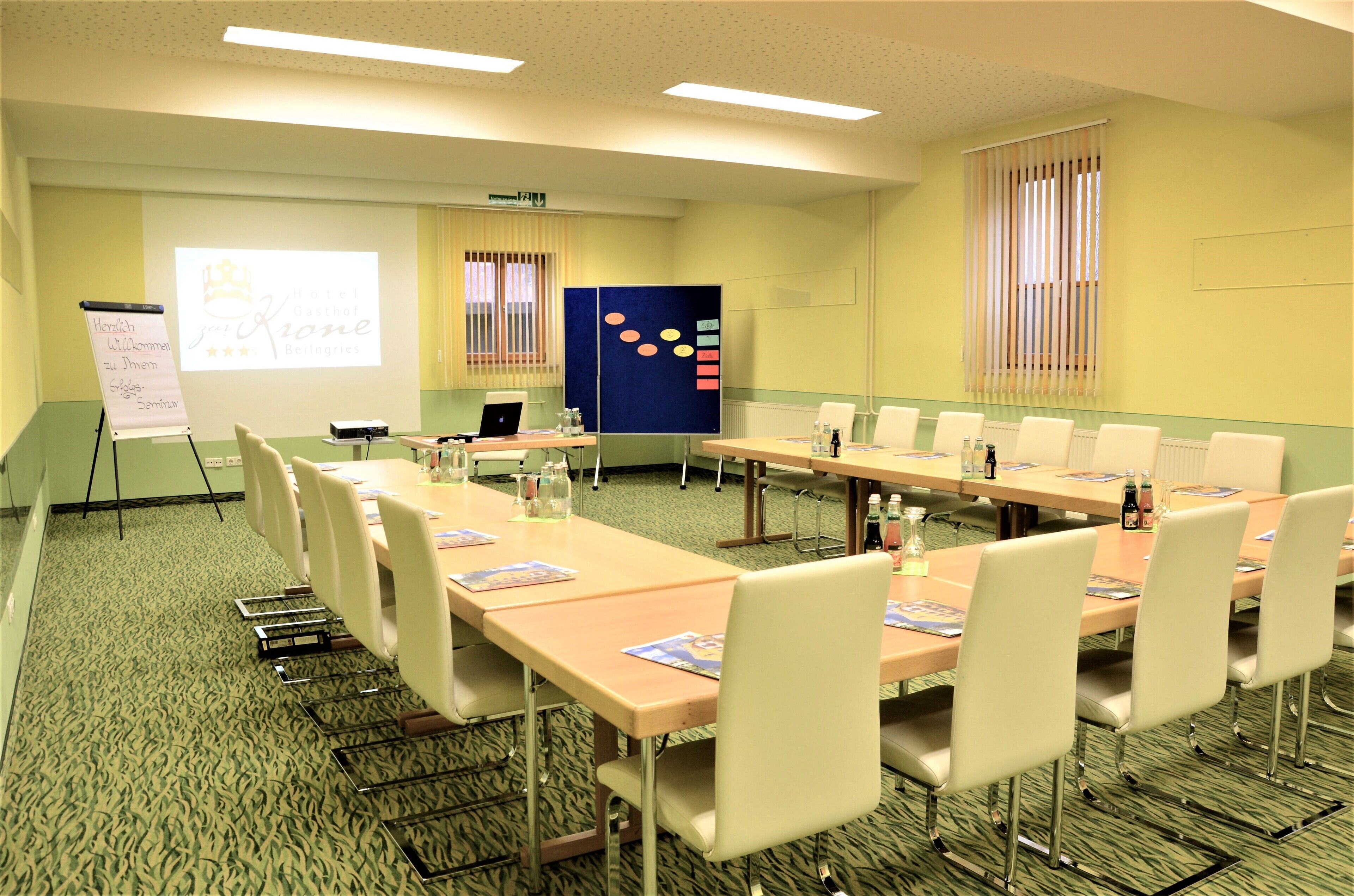 Une salle de conférence avec de longues tables, des chaises blanches et un écran de projection.